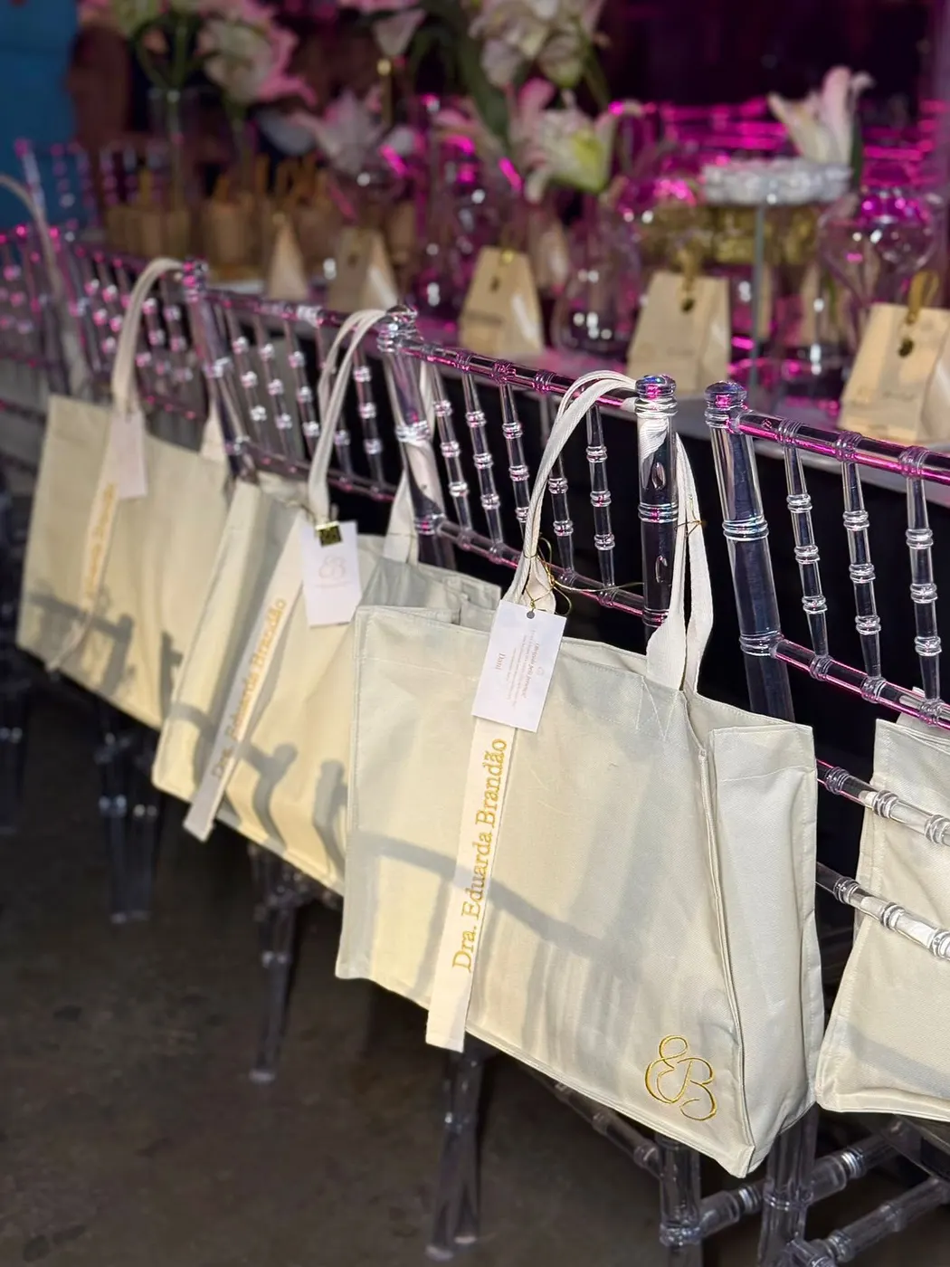 Bolsas cru com tags penduradas nas cadeiras de acrílico de um evento