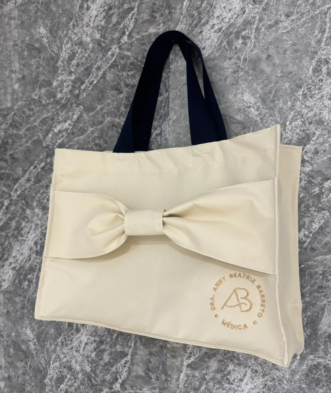 Bolsa cru modelo Laço com alças marinho e emblema circular “Dra. Anny Beatriz Barreto, médica” bordado em dourado
