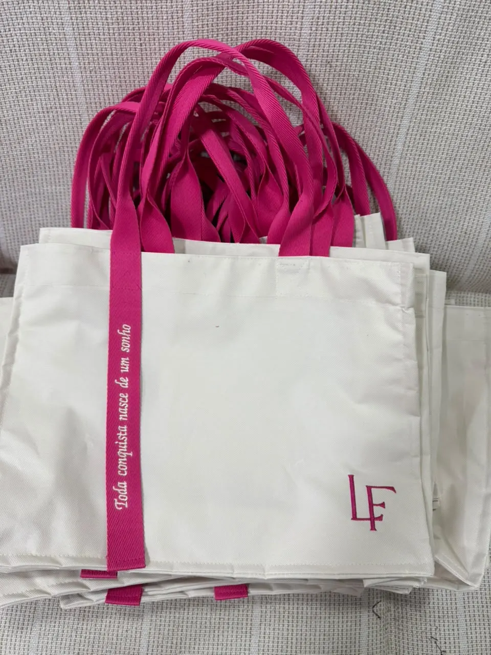 Lote de bolsas cru com alças pink e a frase “Toda conquista nasce de um sonho”