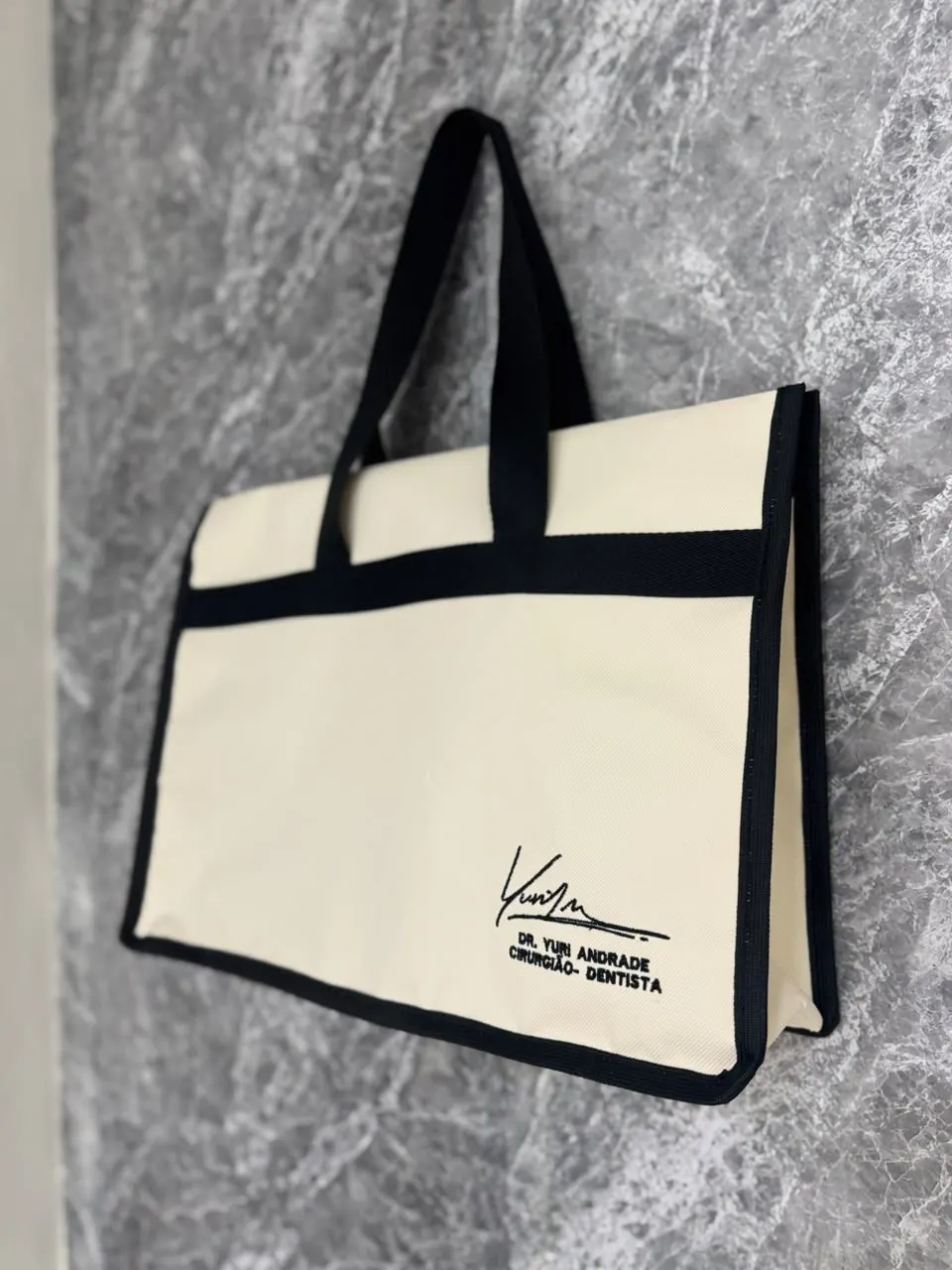 Bolsa cru modelo Moldura com viés e alças pretas e assinatura do Dr. Yuri Andrade, cirurgião-dentista